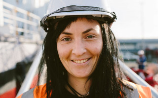 A lady wearing a hard hat, and a high-vis vest, smiles on a boat