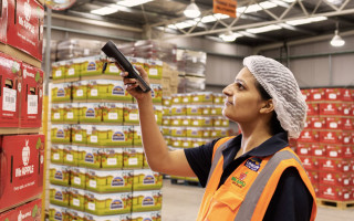 A woman scans a box of apples in a warehouse